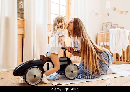 Eine junge Mutter küsst ihre kleine Tochter, während sie zu Hause spielt. Familienleben in der Freizeit Stockfoto