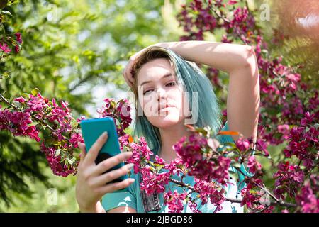 Blauhaarige Frau hat Selfie gegen den Frühlingsblütenbaum gemacht. Stockfoto