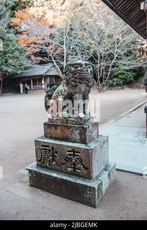 Komainu (löwenförmiger Schutzhund) Statue im alten Schrein in Fukuoka, Japan. Die japanischen Wörter, die auf dem Sockel geschnitzt wurden, bedeuten „Votivopfer“. Stockfoto