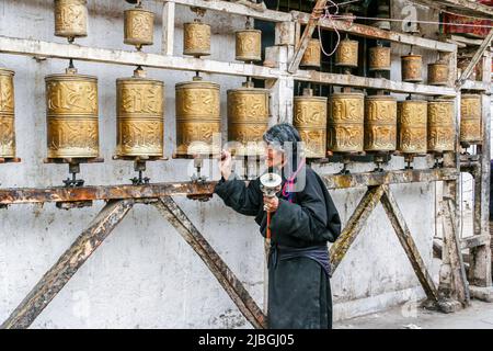 Eine Tibeterin dreht die Gebetsräder auf der Barkhor Street in Lhasa, Tibet. Stockfoto