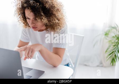 Seriöse Frau, die bei der Arbeit zu Hause auf den Laptop zeigt Stockfoto