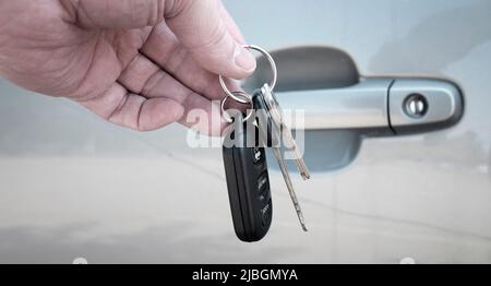 Hand hält die Autoschlüssel vor der grauen Autotür Stockfoto