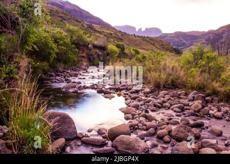 Ruhiger Blick über den Cowl Fork River in der Abenddämmerung, mit dem Mönchs Cowl Peak im Hintergrund, Drakensberg Mountains, Südafrika Stockfoto