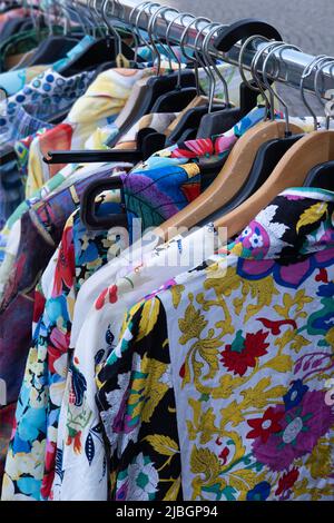 Auf dem Freiluftmarkt in Maastricht hängen eine nach der anderen billige bunte Sommerkleider an Holz- und Kunststoffbügeln. Konzentriere dich auf das Kleid vorne Stockfoto