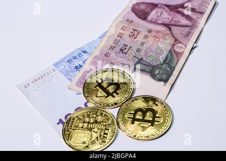 Nahaufnahme der südkoreanischen Won-Scheine (KRW) mit Bitcoins auf weißem Hintergrund. Stockfoto