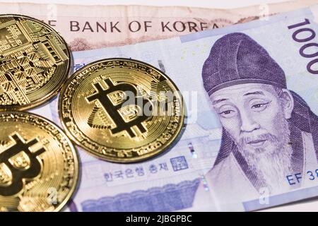 Nahaufnahme der südkoreanischen Won-Scheine (KRW) mit Bitcoins auf weißem Hintergrund. Stockfoto