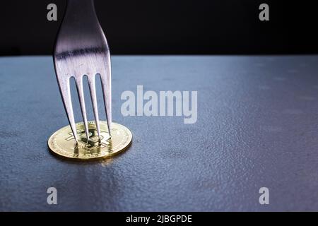 Konzeptbild der Bitcoin-Hartgabel (Blockkette). Silberne Gabel stechend goldener Bitcoin. Kryptowährung Münze unter der Gabel ist auf dem Tisch im Dunkeln. Stockfoto