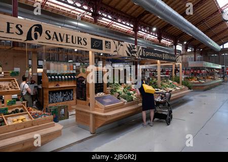 Frau mit gutherzigen Buggy schaut auf die Obst- und Gemüseabteilung in der überdachten Markthalle in Colmar im Elsass. Lokale und Bio-Produkte Stockfoto