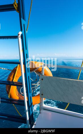 Schiffsheck, Rettungsleine. Fußabdruck auf dem Wasser vom Boot aus. Blaues Wasser und Berge am Horizont. Issyk-Kul, Kirgisistan Stockfoto