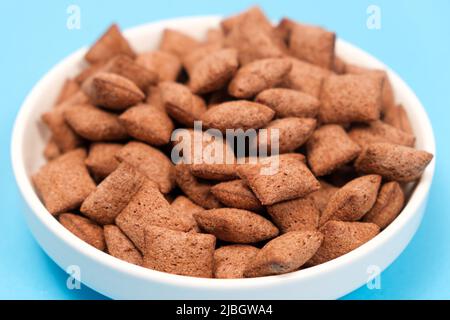 Süßes Frühstück, Müsli, trocken – Schokoladenkissen aus Müsli auf blauem Hintergrund, Seitenansicht Stockfoto