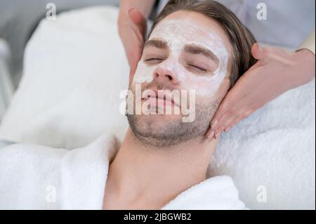 Junger Mann mit Maske auf seinem Gesicht mit Nackenmassage Stockfoto