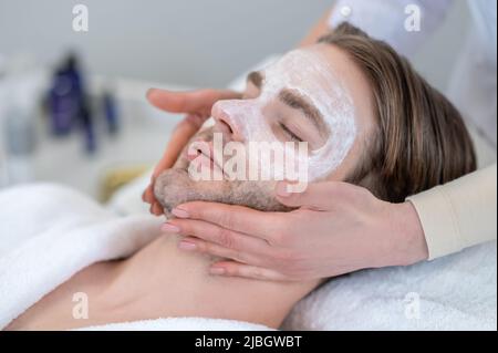 Junger Mann mit Maske auf seinem Gesicht mit Nackenmassage Stockfoto