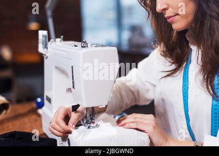 Junge Modedesignerin, die in einer Werkstatt an einer Nähmaschine arbeitet. Stockfoto