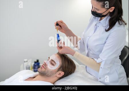 Kosmetikerin im Salon, die Serum auf das Gesicht der männlichen Stollen appt Stockfoto