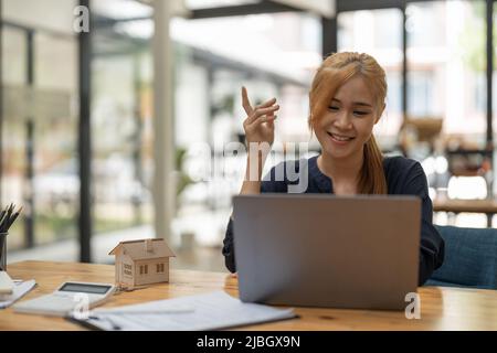 Suchen im Internet nach Immobilien oder neues Haus mit Modell zu Hause und Schlüssel, junge asiatische Frau mit Laptop-Computer. Stockfoto