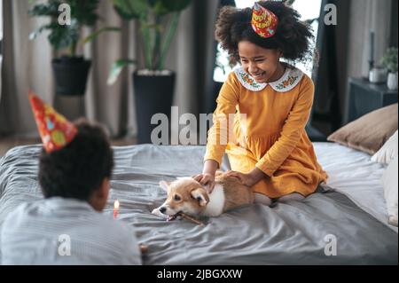 Zwei Kinder feiern den Puppenbundtag und bieten ihm einen Pfannkuchen an Stockfoto