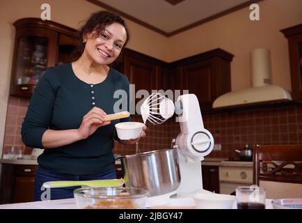 Charmante afroamerikanische Frau, Hausfrau, Konditorei mit Mascarpone-Käse und Keksen, lächelt beim Zubereiten des Homemas vor der Kamera Stockfoto