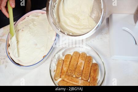 Schritt für Schritt Prozess der Herstellung von italienischen Dessert Tiramisu aus savoiardi Keks, Mascarpone-Käse, Espresso-Kaffee auf weißem Tischtuch Backgro Stockfoto