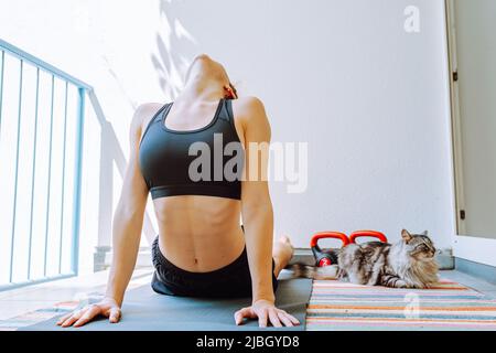 Weibliche Athletin, die einen Kettle-Bell-Swing durchführt. Junge Frau macht Yoga-Training oder Stretching zu Hause Stockfoto