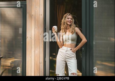 Fröhliche blonde Frau, die am Hauseingang steht Stockfoto