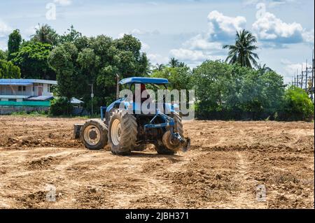 Landwirt, der einen blauen Traktor fährt, um Ackerboden auf landwirtschaftlichem Gebiet zu pflügen Stockfoto