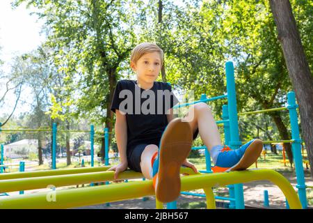 Junge, der auf Gymnastikbars im Park sitzt Stockfoto