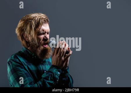 Männlich besucht Karaoke. Bärtiger Mann, der mit Mikrofon singt. Männlicher Gesang mit Mikrofonen. Mann mit einem Bart, der ein Mikrofon hält und singt. Bärtig Stockfoto