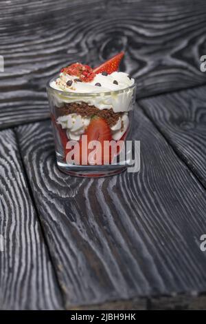 Dessert mit Erdbeeren und Rahm. In einem Glasgefäß. Auf schwarzen Kiefernbrettern. Nahaufnahme. Stockfoto