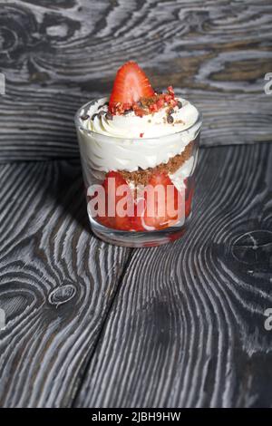 Dessert mit Erdbeeren und Rahm. In einem Glasgefäß. Auf schwarzen Kiefernbrettern. Nahaufnahme. Stockfoto