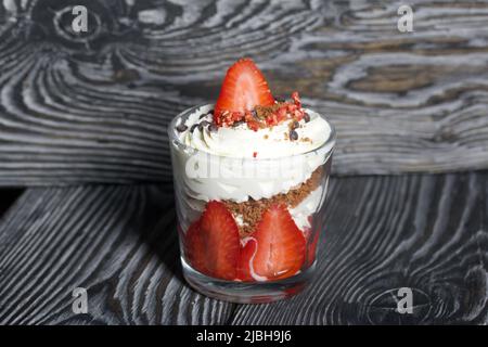 Dessert mit Erdbeeren und Rahm. In einem Glasgefäß. Auf schwarzen Kiefernbrettern. Nahaufnahme. Stockfoto