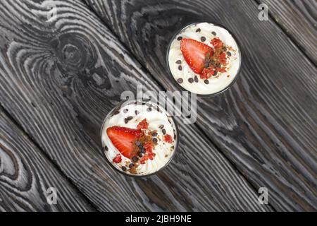 Dessert mit Erdbeeren und Rahm. In einem Glasgefäß. Auf schwarzen Kiefernbrettern. Nahaufnahme. Stockfoto