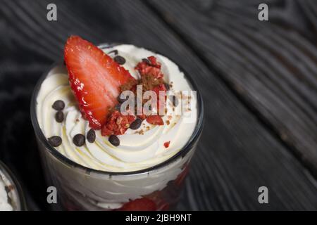 Dessert mit Erdbeeren und Rahm. In einem Glasgefäß. Auf schwarzen Kiefernbrettern. Nahaufnahme. Stockfoto