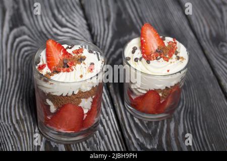 Dessert mit Erdbeeren und Rahm. In einem Glasgefäß. Auf schwarzen Kiefernbrettern. Nahaufnahme. Stockfoto