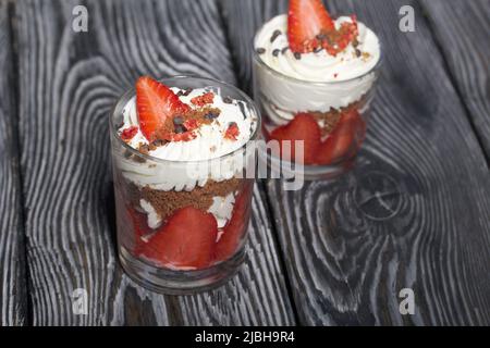 Dessert mit Erdbeeren und Rahm. In einem Glasgefäß. Auf schwarzen Kiefernbrettern. Nahaufnahme. Stockfoto