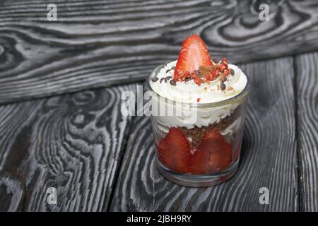 Dessert mit Erdbeeren und Rahm. In einem Glasgefäß. Auf schwarzen Kiefernbrettern. Nahaufnahme. Stockfoto