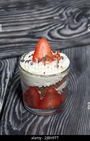 Dessert mit Erdbeeren und Rahm. In einem Glasgefäß. Auf schwarzen Kiefernbrettern. Nahaufnahme. Stockfoto