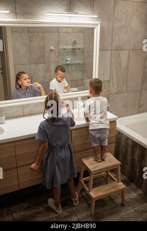 Vertikales Porträt von zwei afroamerikanischen Kindern, die im Badezimmer mit dem Spiegel Zähne putzen Stockfoto
