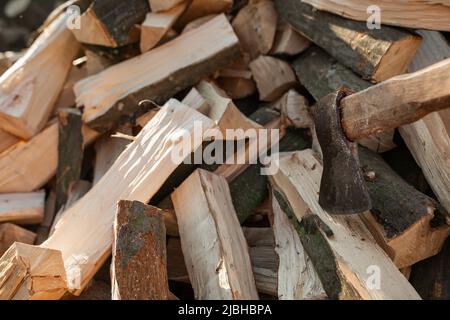 Die Axt ragt in einem Balken auf einen Haufen Brennholz für den Ofen. Landwirtschaft Stockfoto