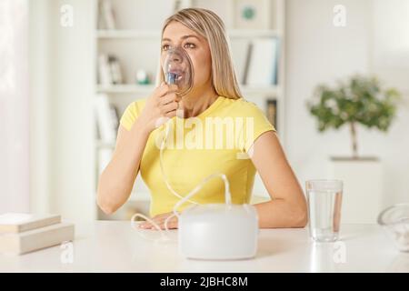Junge Frau, die zu Hause auf einem Tisch sitzt und einen Inhalator benutzt Stockfoto