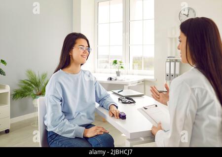 Der Arzt spricht mit einer jungen Patientin, die das Pulsoximeter mit der Fingerspitze in der Arztpraxis verwendet. Stockfoto