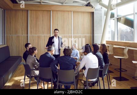 Team von Mitarbeitern, die im Büro sitzen, sich mit dem Business Coach treffen und seinem Vortrag zuhören Stockfoto