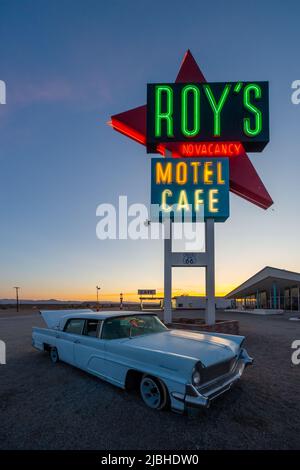 Roy's Motel and Cafe an der Route 66, Amboy, California, USA. Leuchtreklame in der Abenddämmerung. Hochformat. Lincoln Continental Mark IV Auto unten Schild. Blauer Himmel Stockfoto