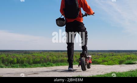Ein junger Mann auf einem Elektroroller, Landschaft von einem Hügel. Leistungsstarker Elektrotransport mit Allradantrieb Stockfoto