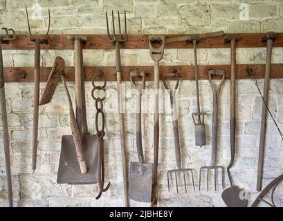 An einer weiß getünchten Wand hängen alte Gartengeräte Stockfoto
