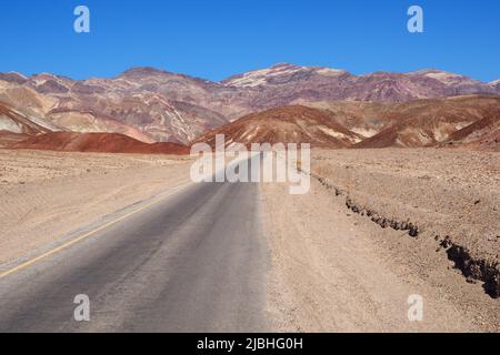 Asphaltstraße führt durch die dampfend heiße Landschaft des Death Valley National Park, Kalifornien, USA. Super heißer sonniger Tag in der Wüste des Südwestens Stockfoto