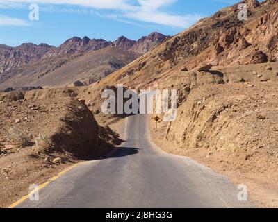 Asphaltstraße führt durch die dampfend heiße Landschaft des Death Valley National Park, Kalifornien, USA. Super heißer sonniger Tag in der Wüste des Südwestens Stockfoto