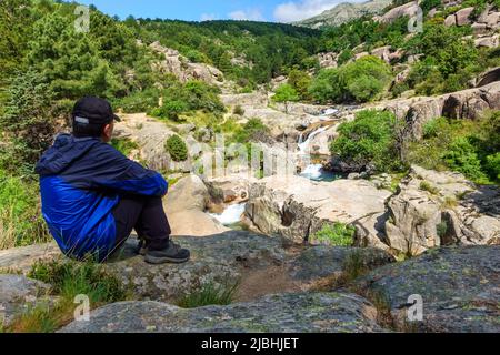 Mann ruht und betrachtet die Landschaft mit Wasserfällen zwischen den Felsen des Berges. Stockfoto