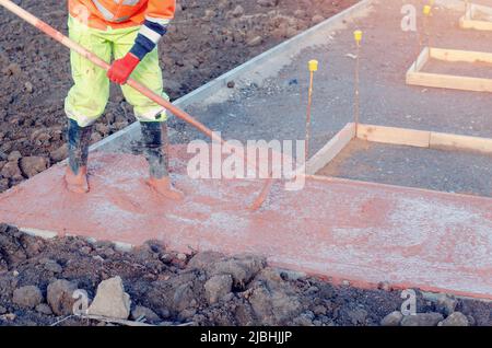 Concreter Spreizung von gegossenem Beton mit einem Rechen oder Spazzle Ein Bauarbeiter nivelliert getönten Beton in Schalungen Stockfoto