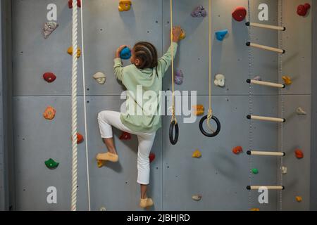 Ganzkörperporträt der aktiven schwarzen Kletterwand für Kinder auf dem Heimsportset, Kopierbereich Stockfoto