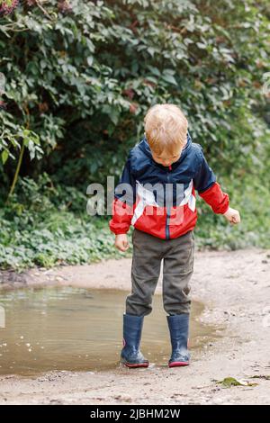 Kind spielt in der Pfütze. Bei schlechtem Wetter spielen Kinder im Freien im Herbst. Herbst Regenwetter Outdoor-Aktivitäten für kleine Kinder. Kind springt im schlammigen Pud Stockfoto